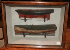 Antique boat hulls in early paint encased in glass display box.
